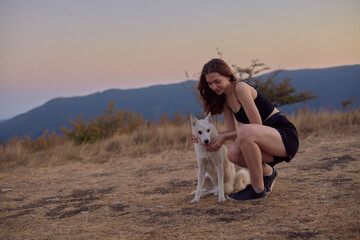 a beautiful, happy woman walks with a white dog in the mountains at sunset