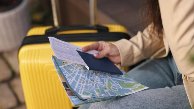 Plane ticket, Solo journey, Itinerary ideas. Ready for travel, woman's hands grip passport, map, and airline ticket, while suitcase rests beside her.