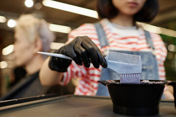 Closeup of hairstylist mixing lightening solution in plastic bowl at beauty salon, copy space