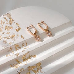 Stylish earrings in 14k pink gold with heart-shaped pendants on plaster figure. Fine jewelry for women, gift for her. 