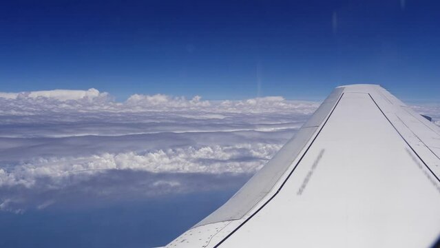 View from the window of an airplane on its wing and white clouds under the blue sky above the ground. Flying an airplane above the clouds. Aerial view