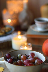 Cup of tea or coffee, plate with desserts, dried oranges, bowl of grapes, scented candles, vintage books, pumpkins and autumn leaves on the table. Autumnal hygge. Selective focus.
