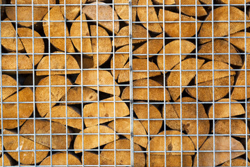 Wooden firewood logs are stacked behind metal mesh. Wood texture and metal lattice.