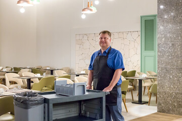 A restaurant worker pushes cart to collect dirty dishes.