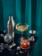 Splash in champagne glass, cocktail glass, shaker, and jigger on black table with Christmas...