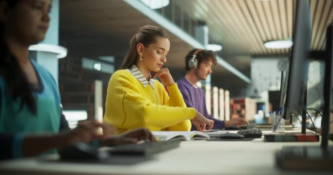 Smart Young Female Studying Hard in a Public Library with Other People. Student Reading Exercise Book, Writing Down Notes in a Notebook and Using a Desktop Computer for Research