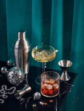 Splash in champagne glass, cocktail glass, shaker, and jigger on black table with Christmas decorations
