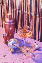 Splash in champagne glass, cocktail glass, shaker, and jigger on pink table with Christmas decorations