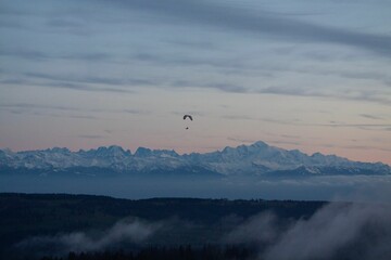 Scenic view of a mountain range with a paraglider in the sky at sunset. Mont d'Or, France.