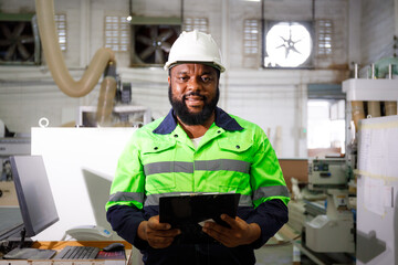 Portrait. African male engineer using a tablet computer. The background is a CNC cutting machine in...