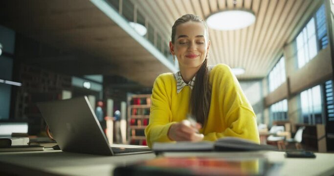 Happy Caucasian Female Student Working on Her Economics School Thesis on a Laptop Computer. Young Smart Woman Sitting Behind a Desk, Brainstorming Business Ideas in a Public Library