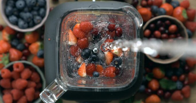 Pouring water into blender in super slow-motion, berries smoothie preparation. Strawberries, cranberries, blueberries inside blender