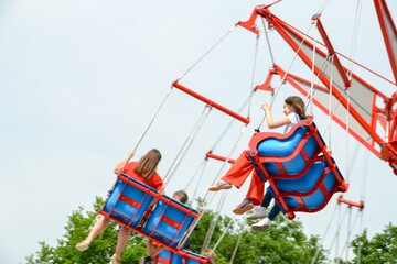 Kids having fun in ferris wheel with chains, carousel ski flyer in amusement park. Happy children,...