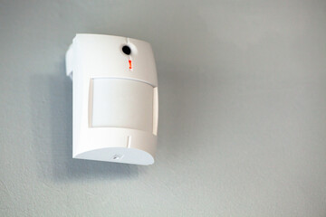 A white motion sensor camera on a gray wall, providing security and surveillance. - obrazy, fototapety, plakaty