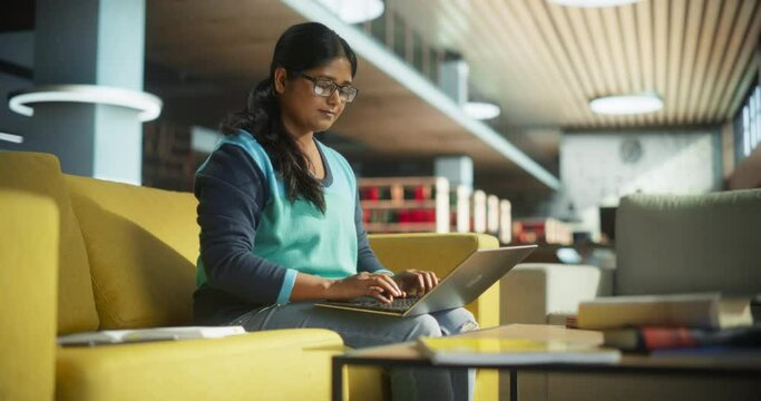 Young Indian Female Specialist Working in a Rest Area in an International Startup Office. Project Manager Holding Her Laptop Computer on a Lap, Browsing Internet, Researching Information Online
