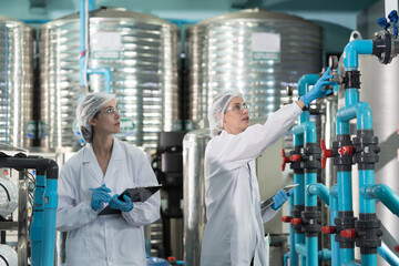 Two female worker wearing uniform, hairnet working and checking of water pump system, pipes...