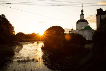 Obraz premium The setting sun illuminates the river bank with an ancient church. An old church on the river bank.