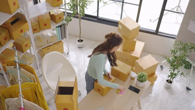 Asian female SME retail store owner Pack products into boxes and prepare them for customers. Fashion designer Startup small business SME concept.