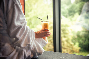 Woman in white bathrobe lying on sofa and relaxing with orange cocktail at SPA.