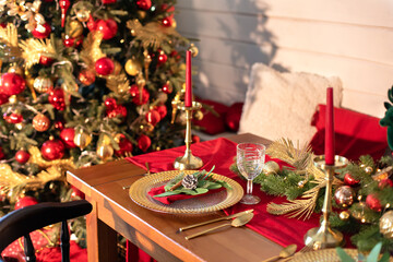 Festive table setting for Christmas dinner at home. Holiday Served table with decorations, candles and garland. Beautiful table setting with Christmas decorations and dishware in living room.	