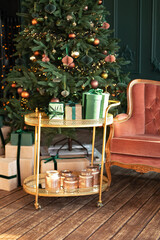 Decorative golden trolley table with gifts and decor. Decorated Xmas tree with lights glowing garlands. Stylish loft living room interior with pink sofa. Christmas at home. New year winter home decor.