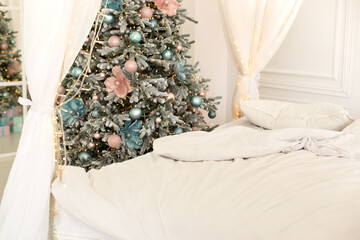Modern white bedroom with bed with flowing white curtains and Christmas tree. Christmas decorated bedroom interior. Bed made with white linens. Morning view of an unmade bed with crumpled linens
