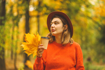 The girl holds a glass of coffee in her hands and enjoys the beautiful autumn weather.