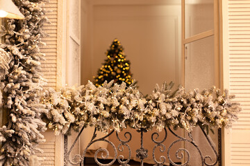 Fototapeta na wymiar Snow covered balcony with wrought french iron railings with open shutters and doors. Old window with wrought-iron balcony decorated branches fir and glowing garland on Christmas 