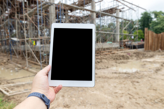 Hand holding digital tablet with empty blank screen on blurred construction site as background.
