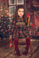 Girl in a Christmas decoration with a lantern in her hand, sitting on a chair.