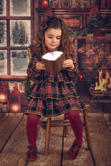 A girl in a Christmas decoration, sitting on a chair looking at a book of light.