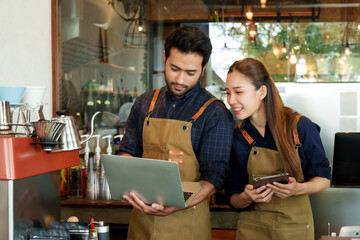 Young barista Asian businesswoman with Indian man They are monitoring sales from laptops and...