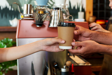 Multiethnic men's hands serving brown disposable paper coffee cups. customer female hand Next to coffee mak coffee maker and coffee equipment shop. small business, personal business Minimal style cafe