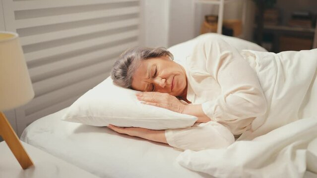 Woman in her 70s waking up in bed, suffering terrible headache, unhealthy sleep
