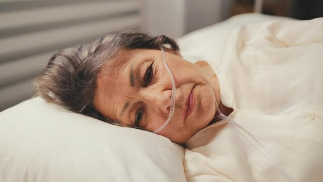 Sad senior woman with nasal cannula lying in bed, suffering asthma, healthcare