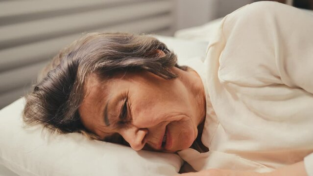 Ill woman in her 70s sneezing and blowing nose in a tissue while lying in bed