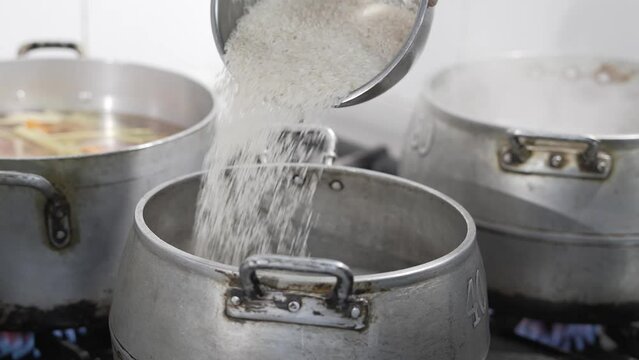 Bowl of rice being poured into the big pot with boiling wiser in the kitchen