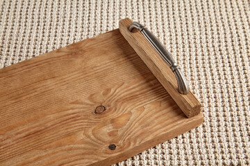 Handmade brown wooden tray with brass handles on a beige knitted tablecloth texture