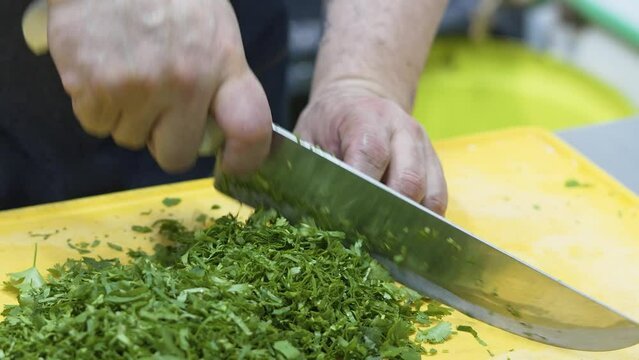 Closeup of a chef cutting the fresh green corianders on the yellow kitchen board with a sharp knife