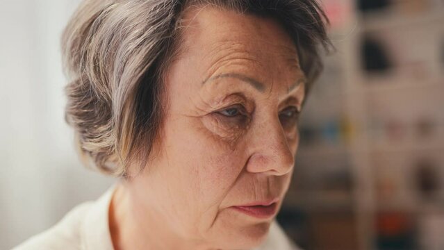 Lonely woman in her 70s looking into empty space, sitting at clinic or hospice