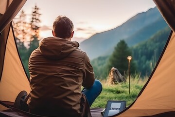 Male traveler camping on the mountain while playing on his phone - obrazy, fototapety, plakaty