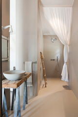 Front view of a tiny restroom with the sink on the right side and a small mirror above it. In the center, there is a shower with a fabric curtain.