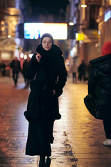 Muslim woman walking on an urban city street on a cold winter night wearing hijab