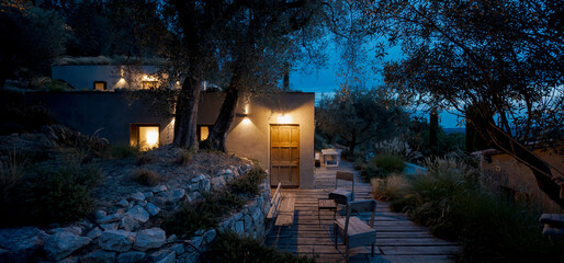 Contemporary house surrounded by olive trees, built on terraced land. Front view in night scene.