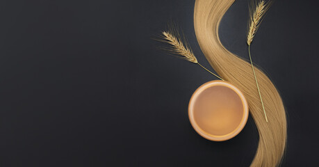 Blond long hair with cream jar and sprigs of ripe wheat. Healthy hair. Black background. Hair...