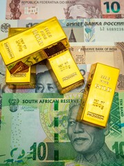 Golden bars on the surface with different currency banknotes © Wirestock