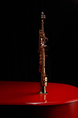 Straight Soprano saxophone on the lid of a red piano in a dark. Copy space. Shallow depth of field. 