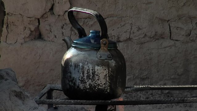 A Rusty Tea Kettle over Fire Against a Mud Wall in a Village in Chaco Province, Argentina. Close Up.