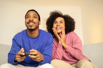 African spouses engrossed in digital video game using gamepads indoor