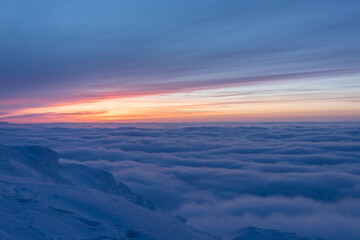 Winter landscape high in the mountains at sunset of the day. The clouds have dropped below the level of the mountain, revealing a stunning view